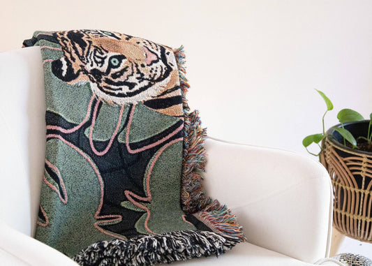 A green and brown Tiger Tapestry Throw Blanket folded on a white chair. A plant is in the background.