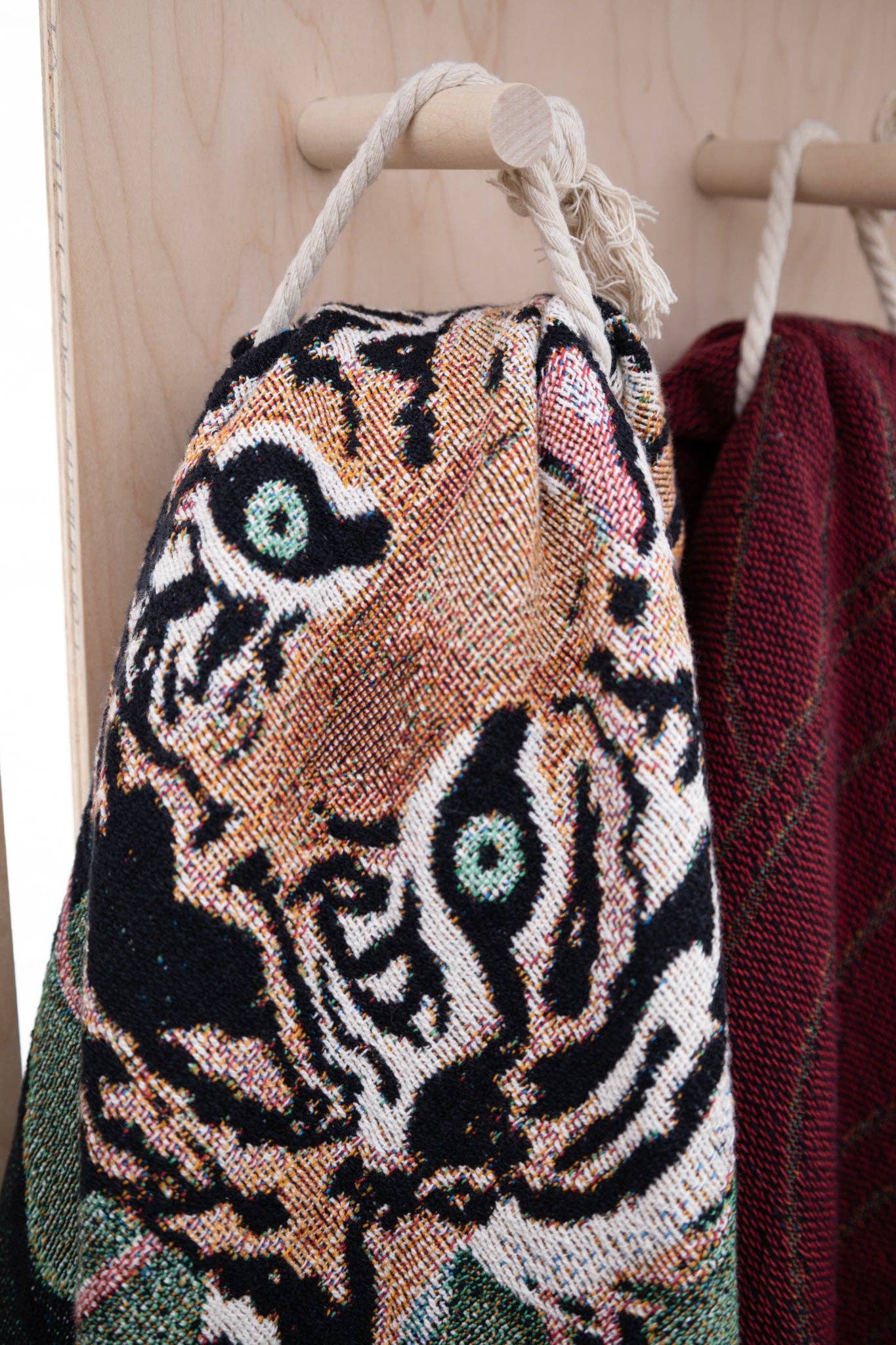 A green and brown Tiger Tapestry Throw Blanket hanging on a hook with a cotton rope.