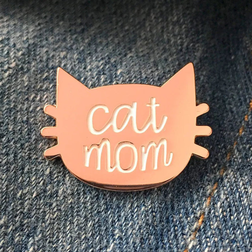 Rose Gold colored cat mom pin on a denim background